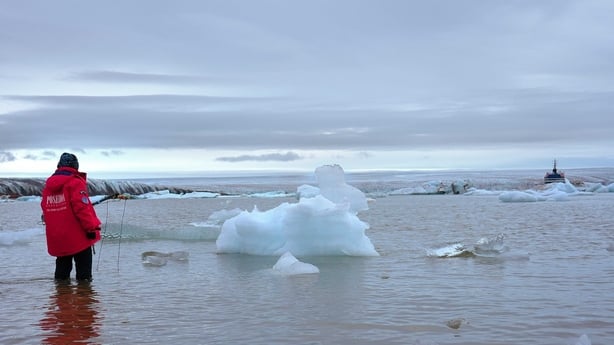 A woman in a red raincoat stands in an icy body of water