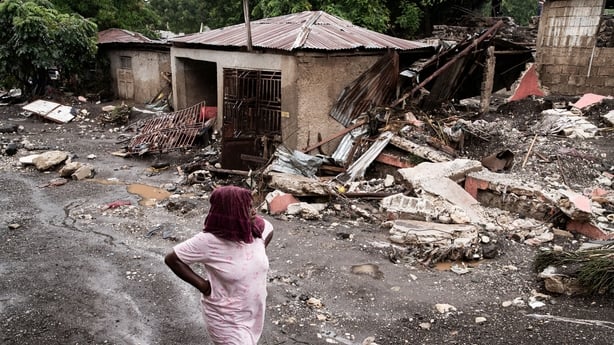 A woman walks past a destroyed home in Haiti