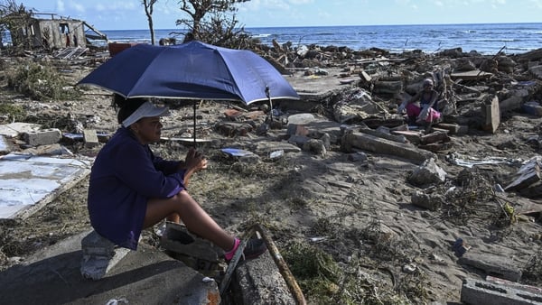 A man with an umbrella is seen resting after hurricane melissa damaged buildings in Dos Rios village