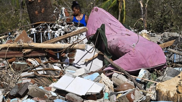 A woman walks amid debris of a damaged house