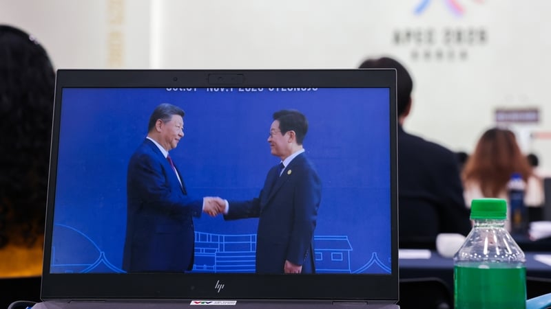 A journalist watches a livestream of Chinese President Xi Jinping being greeted by South Korean President Lee Jae-Myung (R) ahead of the APEC summit