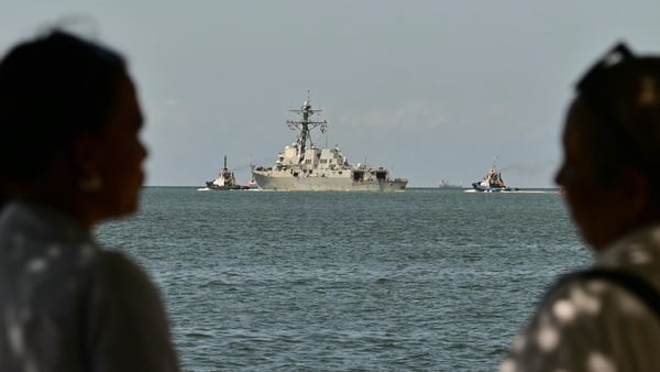 People watch the USS Gravely, a US Navy warship, departing the Port of Port of Spain.