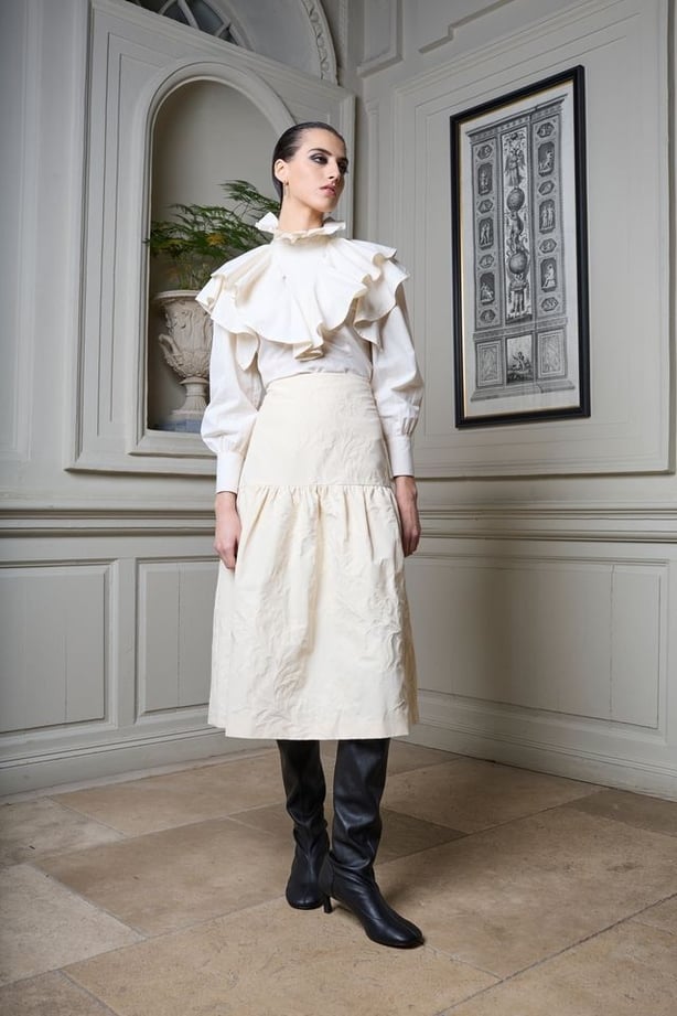 A woman wearing a white blouse and skirt with black boots