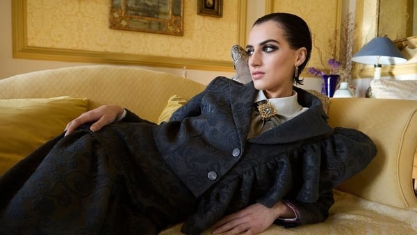 A woman wearing a skirt suit with a white shirt and an ornate brooch at the collar