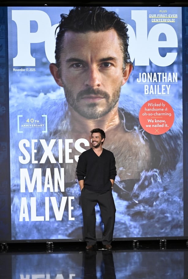 Jonathan Bailey standing in front of a People Magazine cover on which he is named Sexiest Man Alive