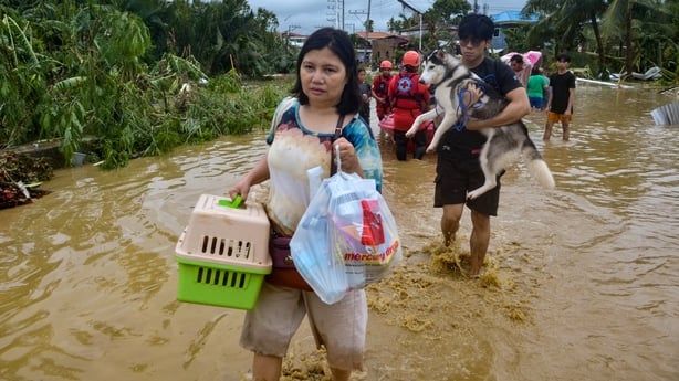 Residents carrying their belongings and pet dogs wade through a flooded street as they evacuate from their inundated homes in Liloan town, Cebu province, on November 4, 2025, after Typhoon Kalmaegi hit overnight. Residents sought refuge on rooftops and cars floated through flooded streets on Novembe