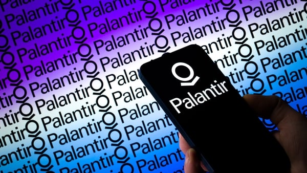 Palantir logo displayed on a mobile phone with the company's branding seen in the background