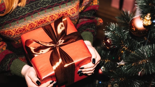 Young woman holding Christmas present standing by Christmas tree at home