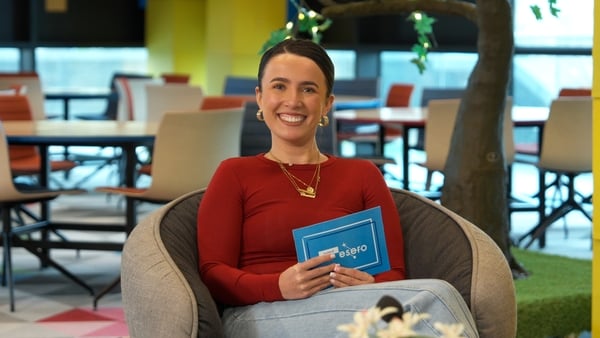 A woman in a red top smiles at the camera on a tv set