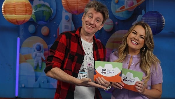 A man and woman pose on a tv set holding cards.
