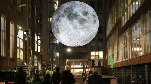 A picture of a museum with a fake moon floating from the ceiling.