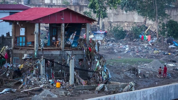 A heavily damaged building with a red roof is seen surrounded by rubble and debris.