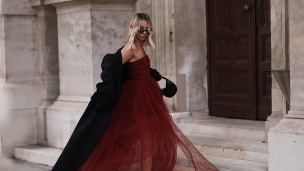 Karin Teigl seen wearing Saint Laurent black sunglasses, H&M Studio red ruffled tulle long bandeau dress, gold necklaces, H&M black wool long coat, Prada black leather handbag and Chanel black logo rubber boots, on November 25, 2023 in Vienna, Austria. (P