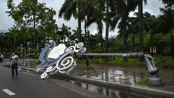 A man talks on a phone next to a lamp post that collapsed in strong winds ahead of the arrival of Typhoon Kalmaegi near Quy Nhon beach in Gia Lai province in Vietnam