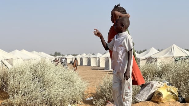 Two children look to the distance in front of two columns of tents at the newly established Al-Afadh camp.