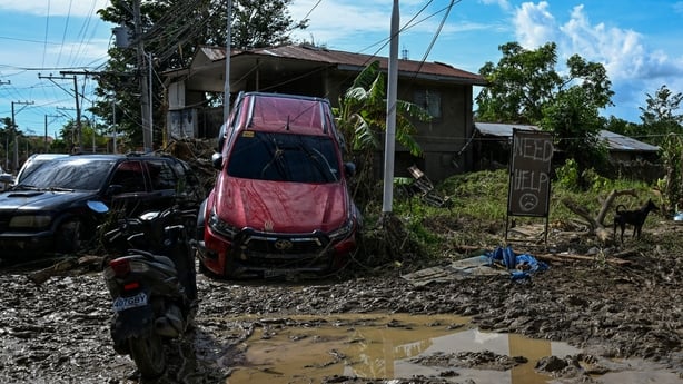 A sign shows the words "Need Help" beside two cars that are impeding upon a house surrounded by mud in Cebu in the Philippines.