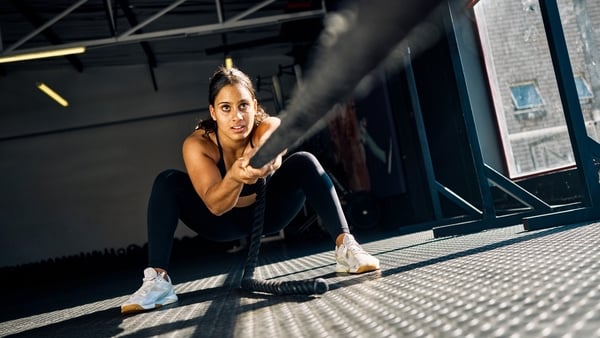 Female athlete pulling a weighted sled in a gym. Front view of a woman performing strength training exercise on a black gym floor. Hyrox Training Concept.