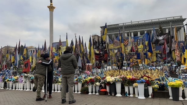 A man and wounded Ukrainian serviceman hug one another at a makeshift memorial in Kyiv