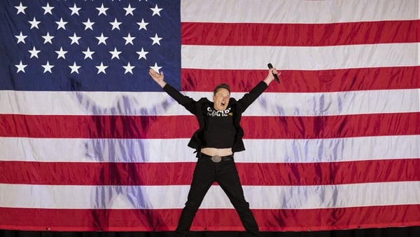 Elon Musk jumps on stage with a giant US flag in the background