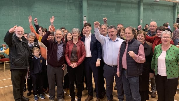 Dozens of people stand in a group cheering and waving their hands.