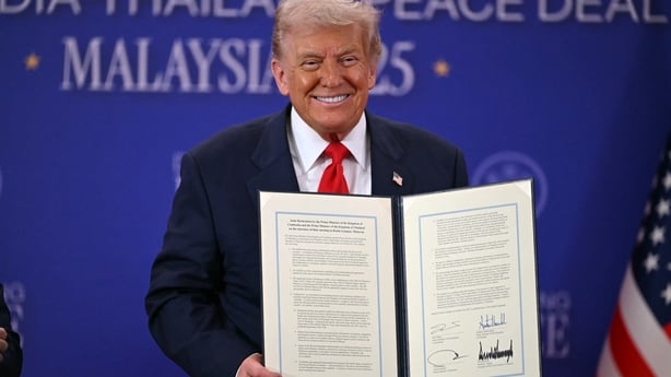 Donald Trump holds a signed document during the ceremonial signing of a ceasefire agreement between Cambodia and Thailand