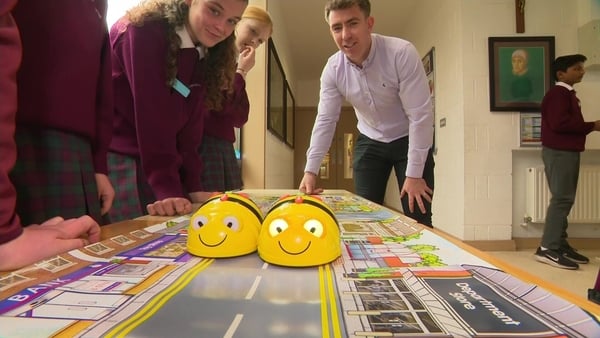 A teacher and two students look on as two robot bees drive along a table top as part of a science exhibition.