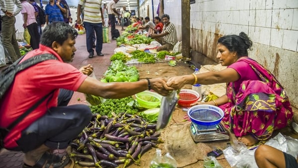 Image of an Indian vegetable seller selling produce inside a subway with people walking by
