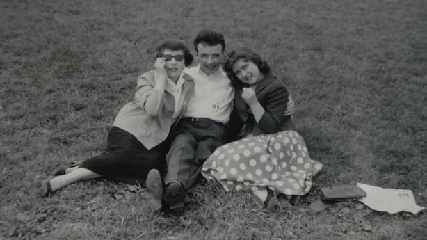 Three people sitting on the grass pose for a photo in black and white