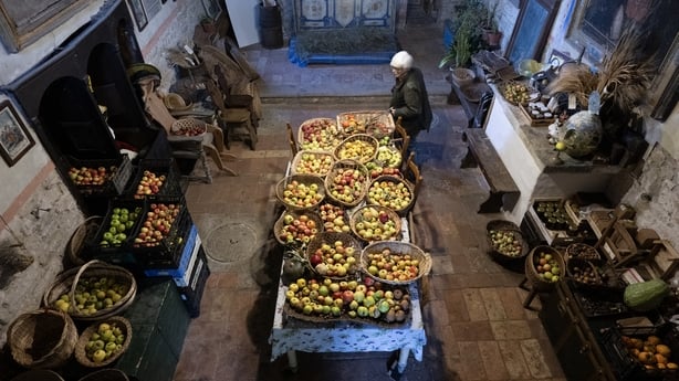 A woman stands in a kitchen beside a table covered in baskets of fruit