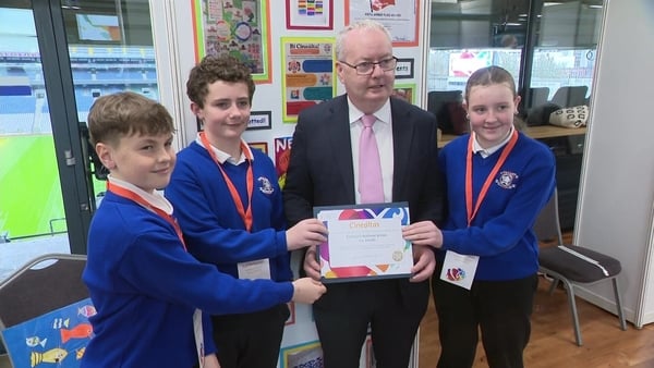 A man presents a certificate to three school children at an exhibition.