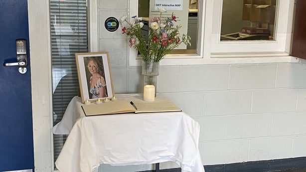 A photo of a young woman is placed on a table with a book of condolence, candles and a vase with flowers