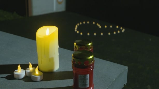 Photo shows candle lights in the shape of a heart with a larger candle lit in the foreground