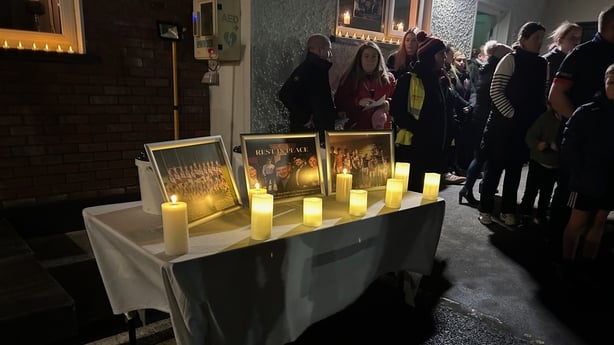 Photographs and candles on a table with people gathered to the side