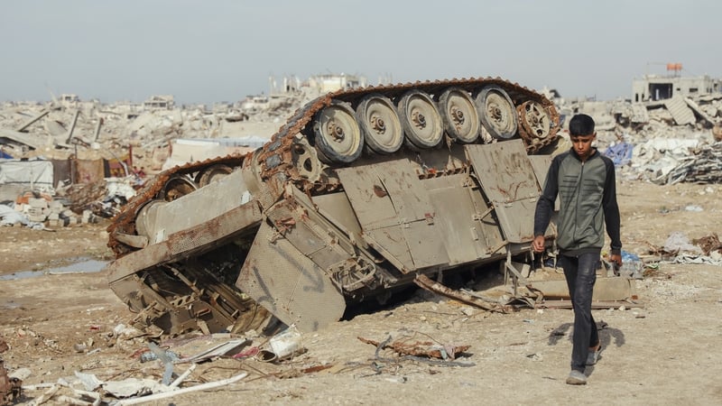 A Palestinian child walks past an overturned tank lying amid widespread destruction in Gaza
