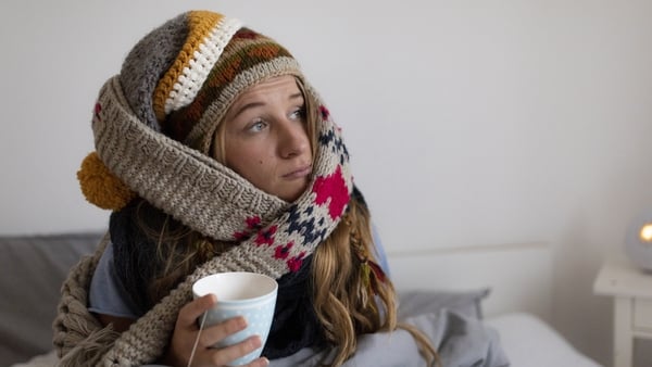 young woman cold sitting in bed drinking tea