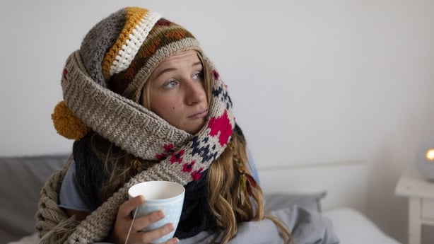young woman cold sitting in bed drinking tea 