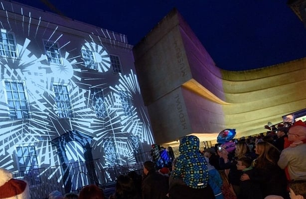 A crowd watches an illumination performance on the front of a building