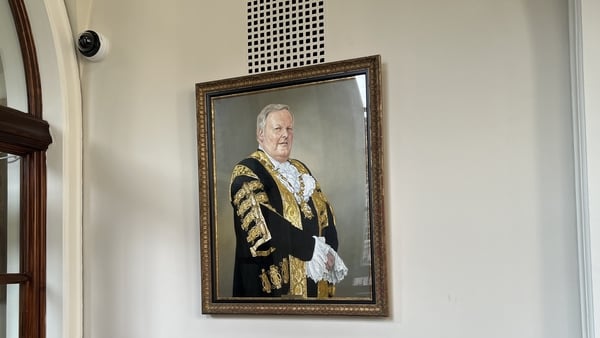 A large portrait of a man wearing ceremonial mayor robes can be seen on a white wall.