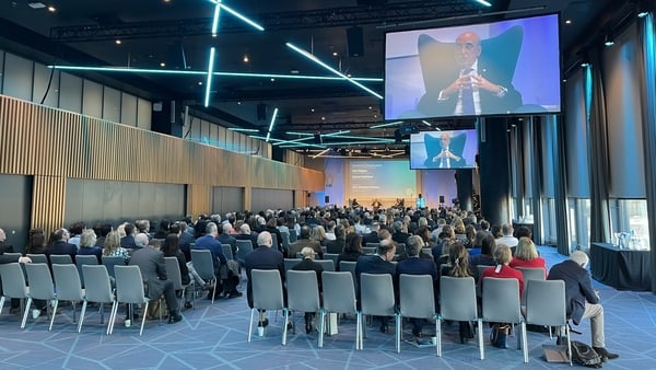 Image of delegates seated at a conference with two big screens showing Central Bank Governor Gabriel Makhlouf