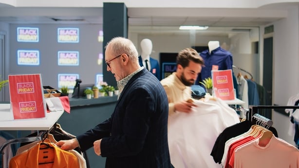 Diverse people shopping in retail store, looking for red black friday discount labels on items. Customers searching through hangers with clothing items in fashion outlet, exploring boutique.