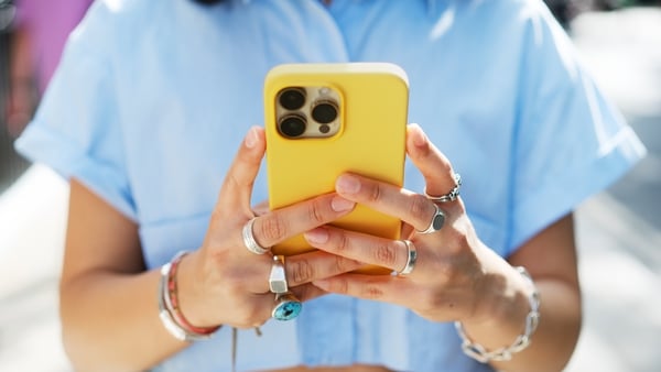 A young woman wearing jewellery holds up her yellow phone