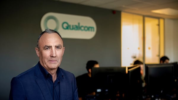 Image of a business man posing in front of the Qualcom logo in an office