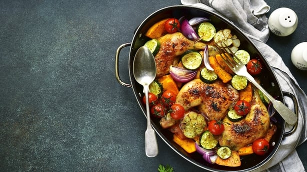 Chicken legs roasted with vegetables in a skillet pan over dark slate,stone or concrete background.Top view.