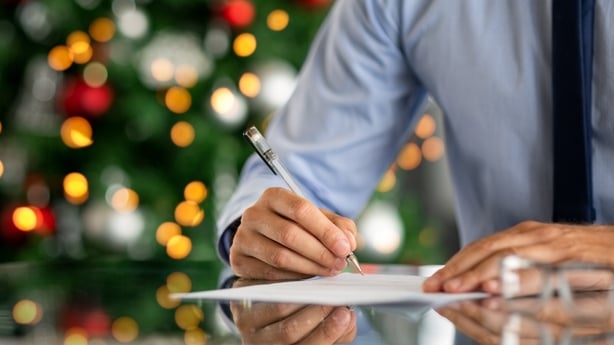 Close up of formal businessman hand signing document in office with decorated christmas tree in background. Close up of man hand signing contract at xmas time. Businessman working on paperwork in office with copy space.
