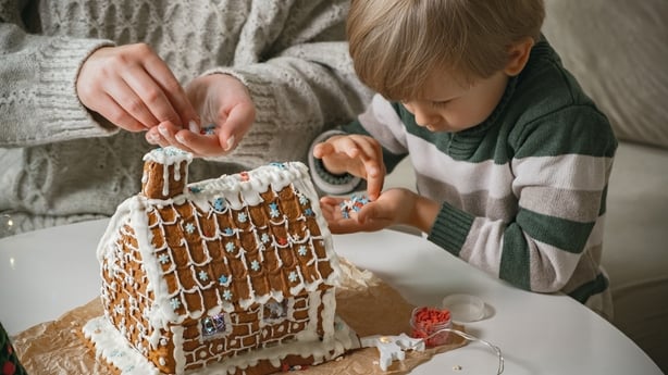 Child with mother decorating christmas gingerbread house together, family activities and traditions on Christmas and New Year's Eve