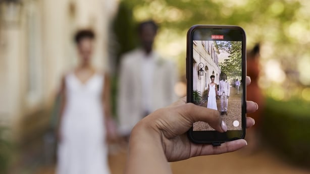 Cropped hand of woman holding smart phone while photographing bride and groom