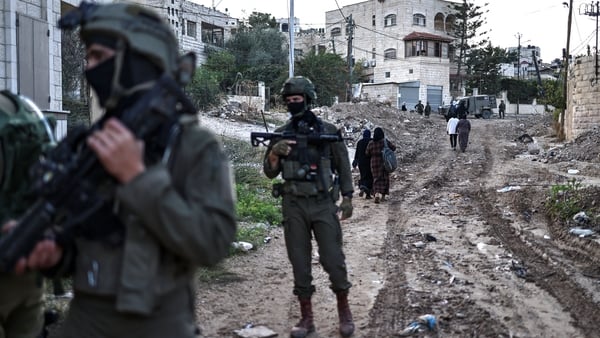 Israeli army troops stand with weapons outside in the West Bank during a raid.