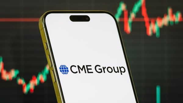 A smartphone displays the logo of CME Group in front of a screen showing the company’s latest stock market chart