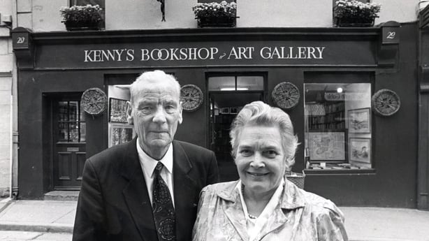 A black and white photo of a man and a woman in front of a bookshop called Kenny's Bookshop and Art Gallery