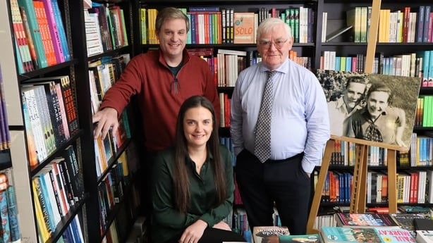 A photo of three people standing in front of bookshelves filled with books